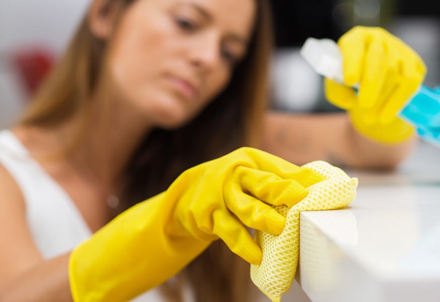 Person som bär gula handskar som rengör en yta med en trasa och sprayflaska.